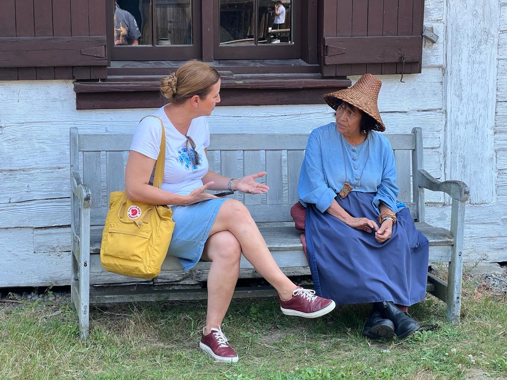 Katarína Slobodová Nováková in conversation with an older woman outside a traditional wooden house during field research