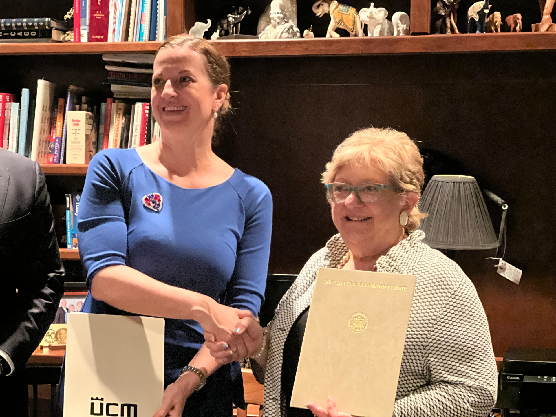 Katarína Slobodová Nováková shaking hands with a representative of the National Czech & Slovak Museum & Library, holding the signed document