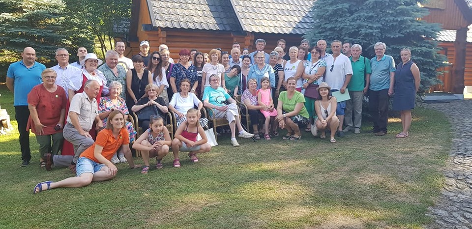 Large outdoor group photograph of the Huncokar community gathered in front of a wooden house