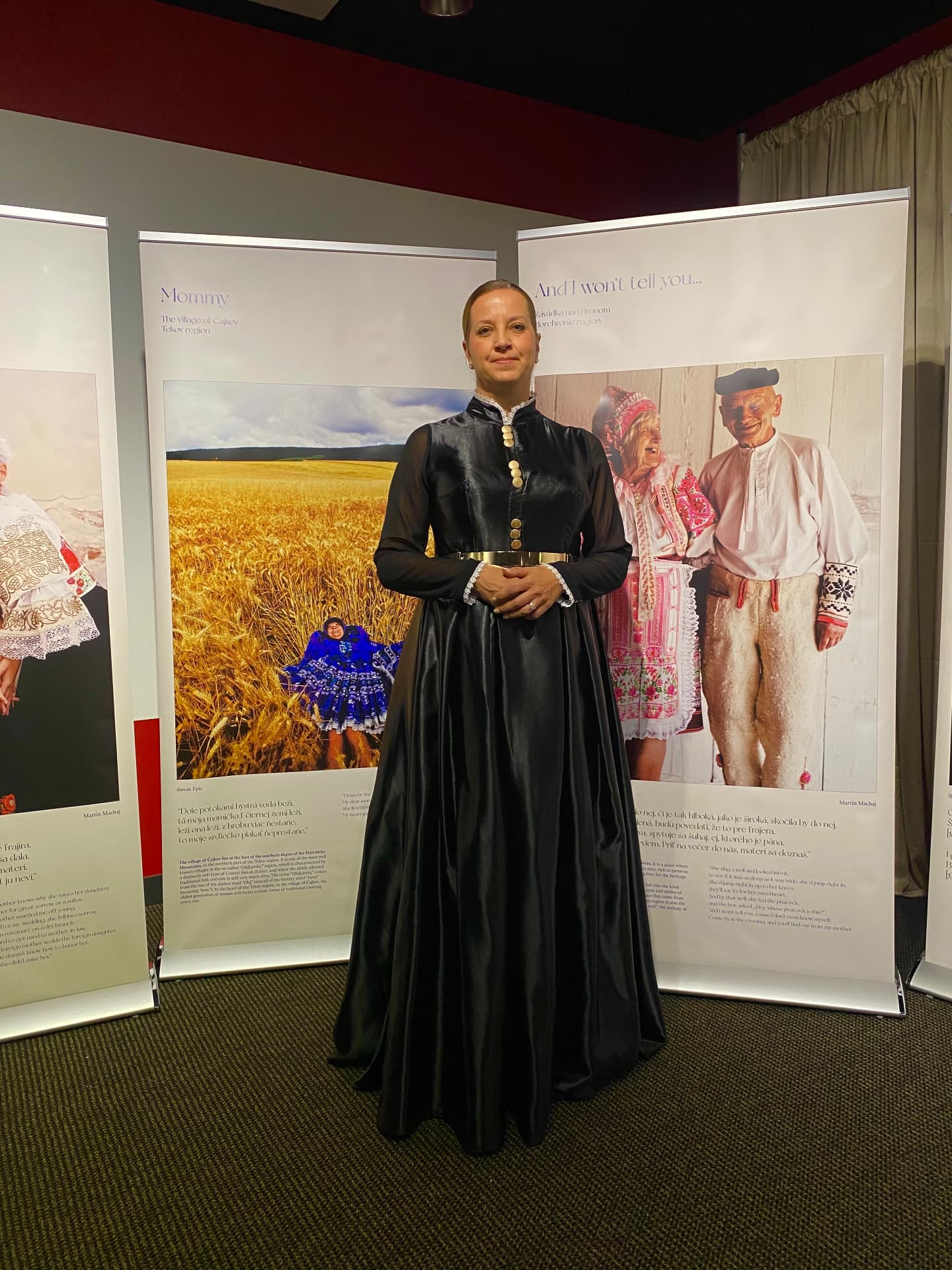Katarína Slobodová Nováková in a dark folk-inspired gown in front of the Slovak Epic exhibition panels