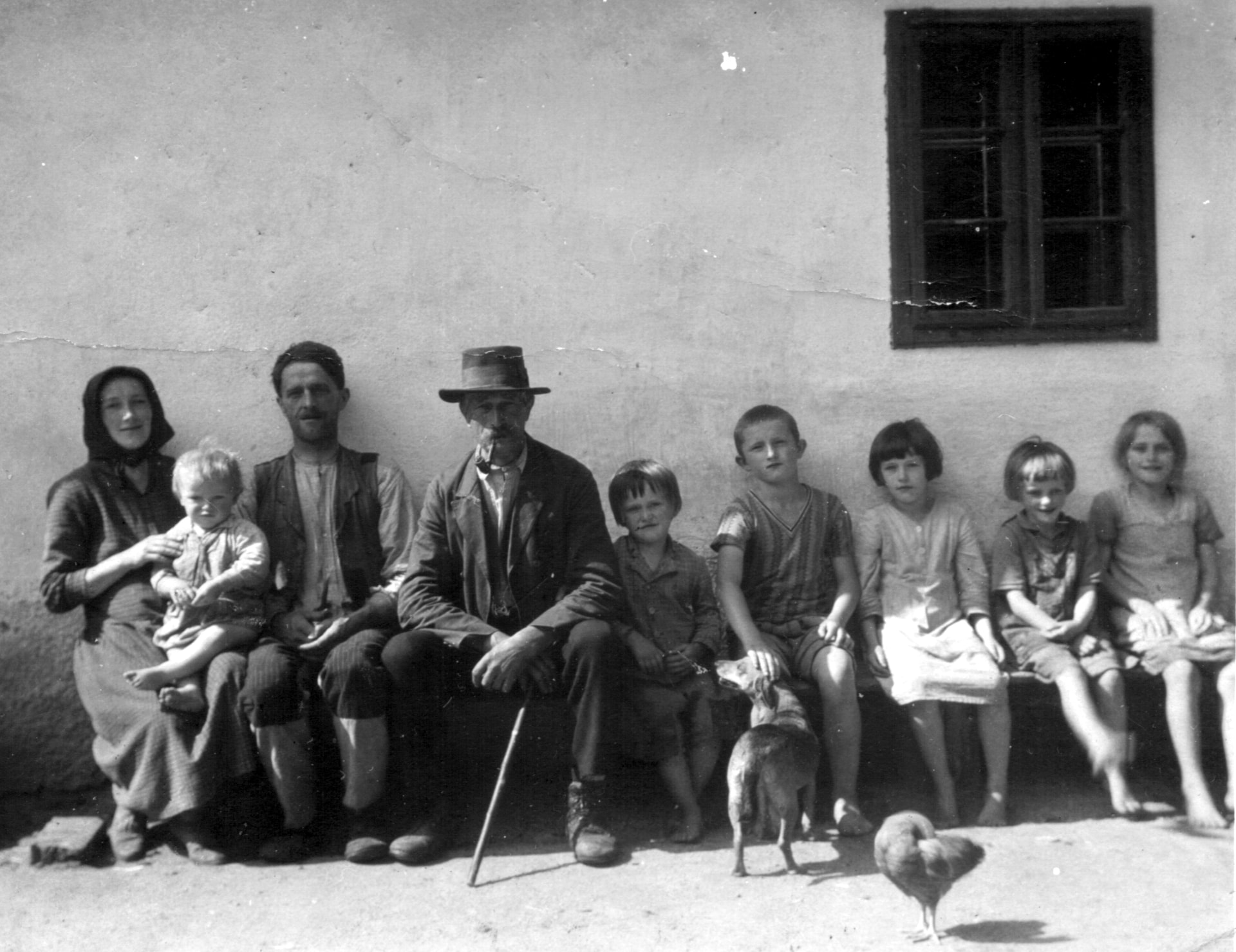 Black-and-white historical photograph of a family seated together in front of a rural house